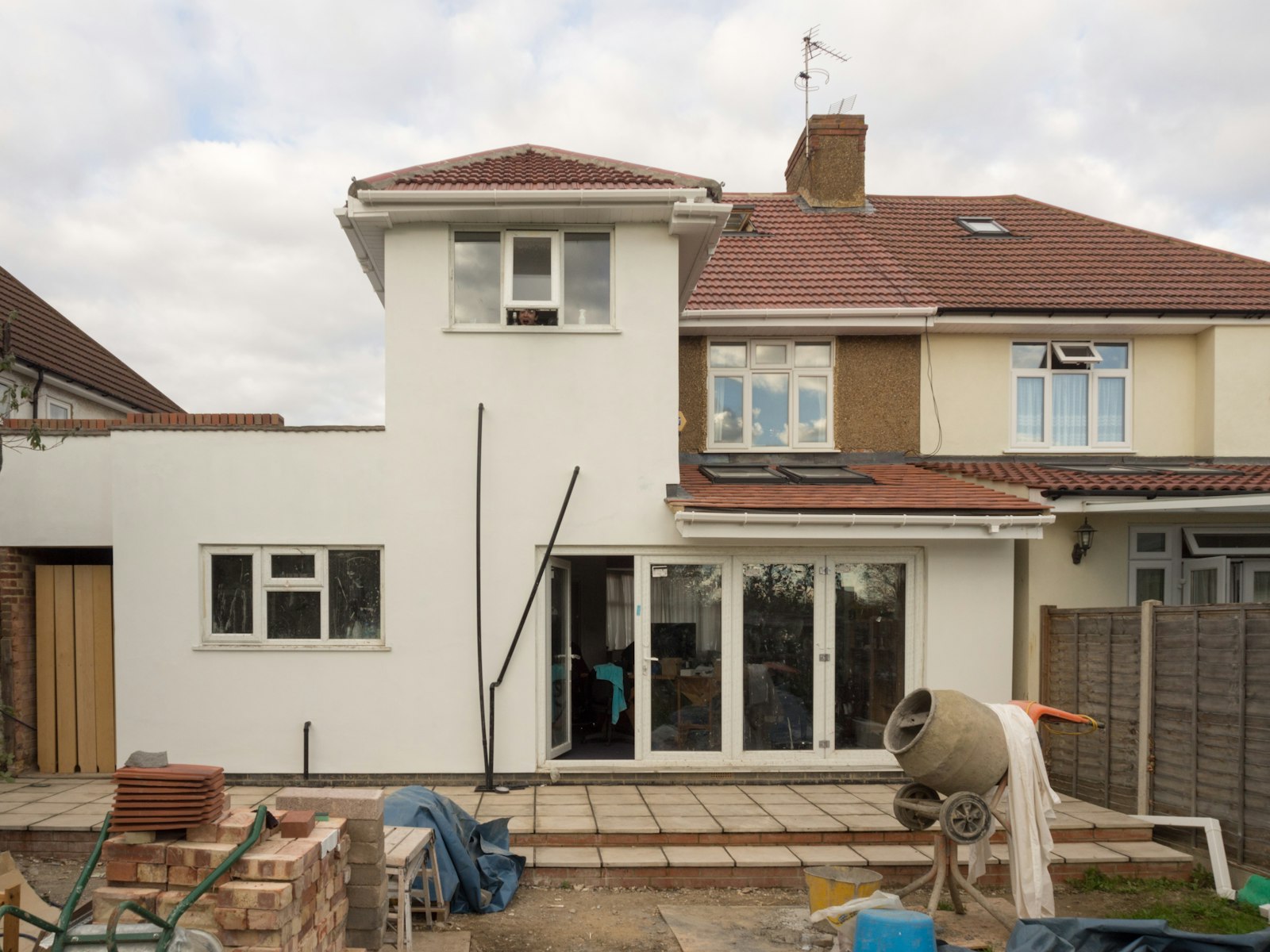 UK builder laying bricks on a single-storey rear house extension with fresh mortar and a spirit level under blue sky